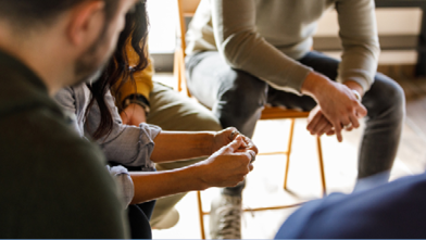 A group sits closely in a supportive circle on chairs, focusing on someone speaking. 