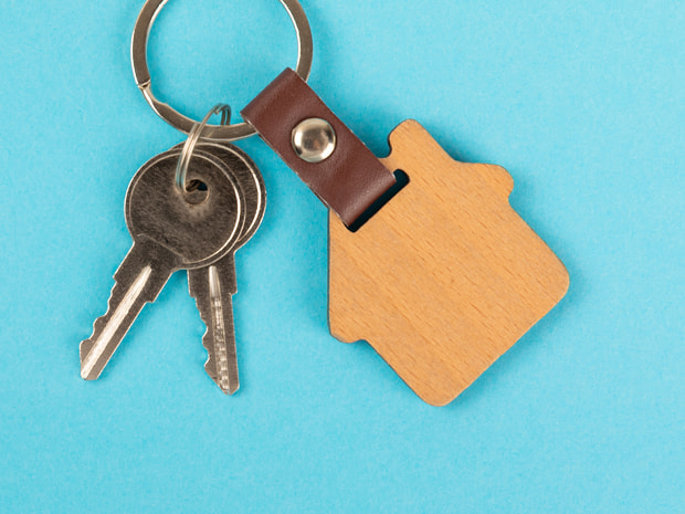A keyring with two metal keys and a wooden house-shaped keychain on a blue background.