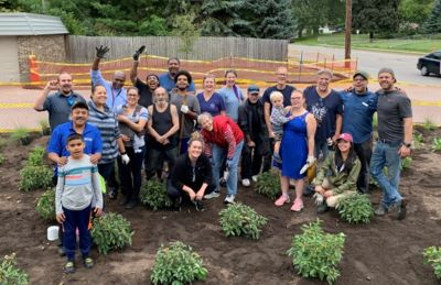 A group of people of multiple generations standing in a newly planted garden celebrating 