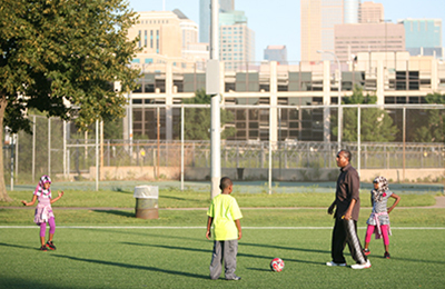 Adult and three kids playing soccer on a field with downtown Minneapolis in the background