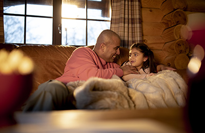 An adult man and his daughter relax on the sofa together.