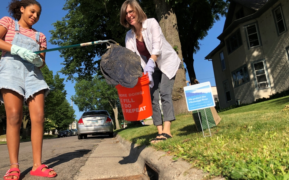 Woman and child using trash grabber to pick up litter from a storm drain.