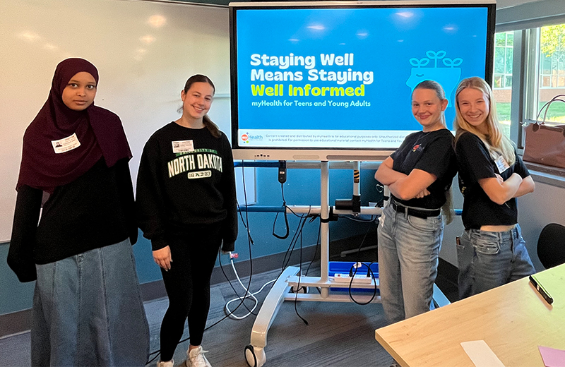 Four kids standing together in school in front of a presentation.